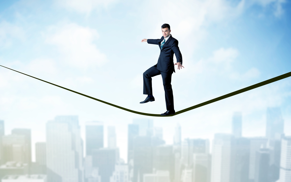 City scape, tall buildings and clouds on clear blue sky with business person balancing on black rope concept