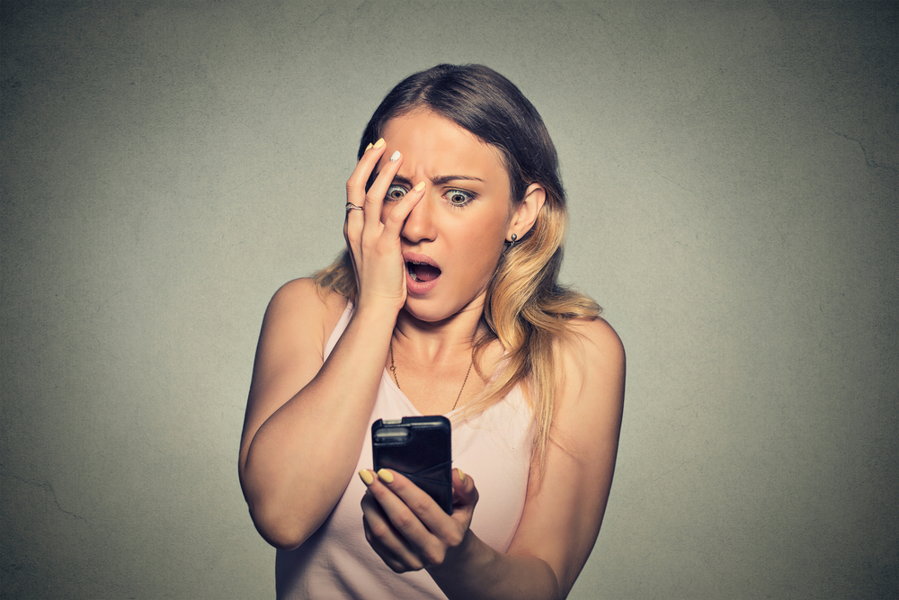 Closeup portrait anxious scared young girl looking at phone seeing bad news photos message with disgusting emotion on her face isolated on gray wall background. Human reaction, expression