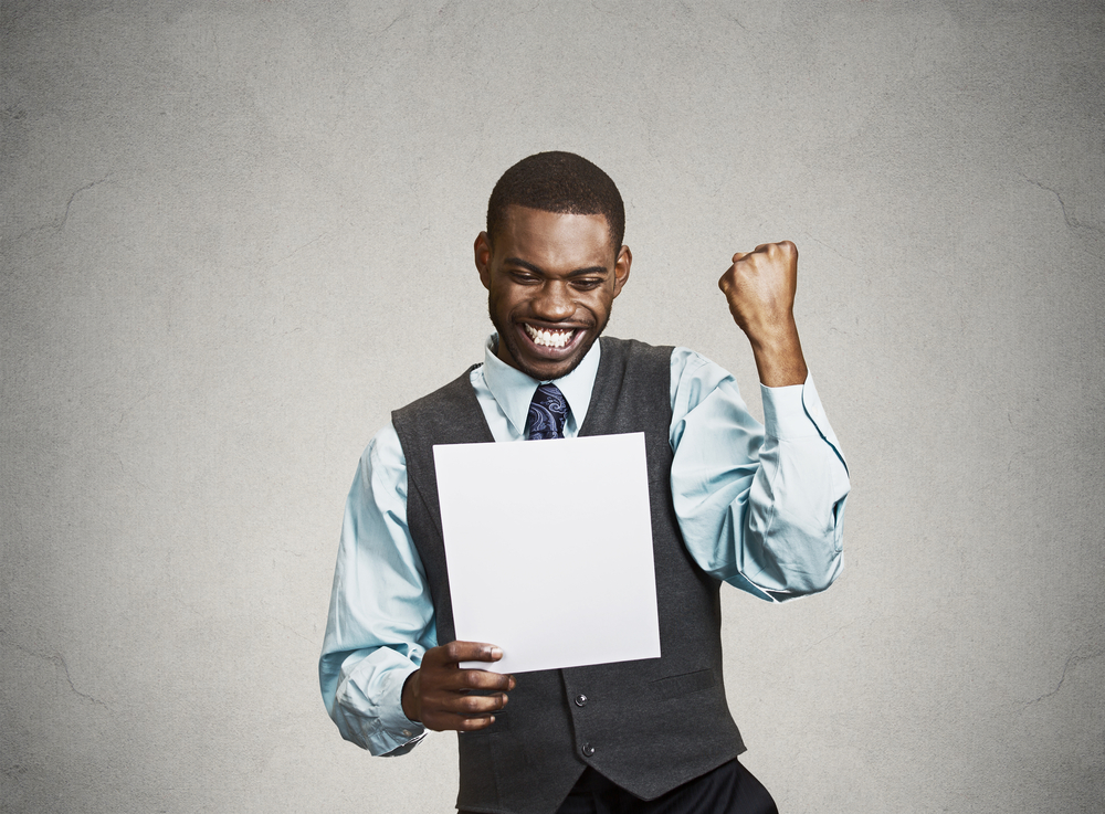 Closeup portrait happy excited young business man executive looking monthly statement glad to pay off bills isolated grey background. Positive emotion facial expression. Financial success good news