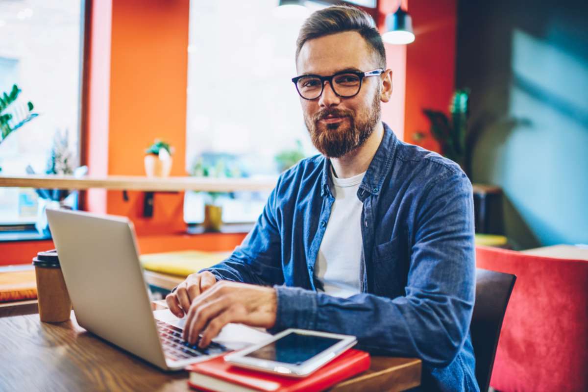 Half length portrait of successful bearded designer smiling at camera while working on freelance at netbook-1