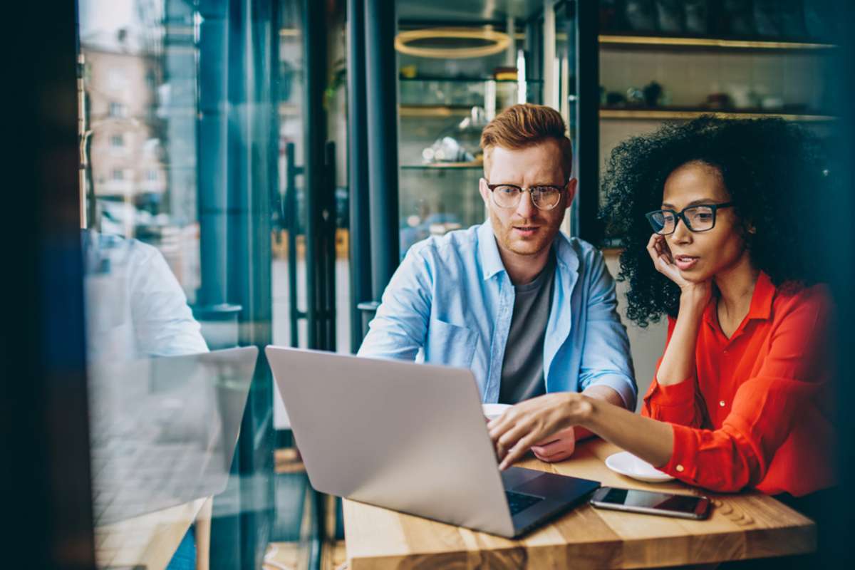 Pensive african american young woman pointing on laptop and explaining task caucasian graphic designer during meeting in coffee shop-1