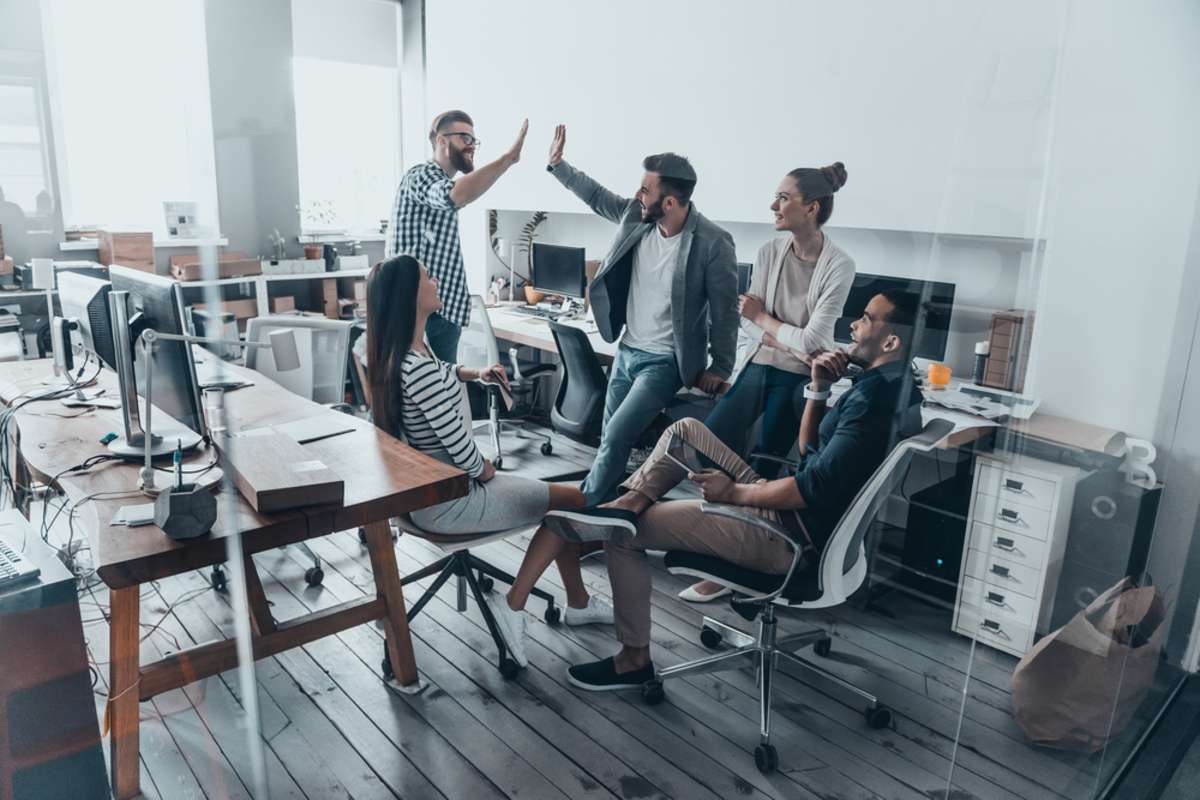 Two cheerful young business people giving high-five while their colleagues looking at them and smiling-1