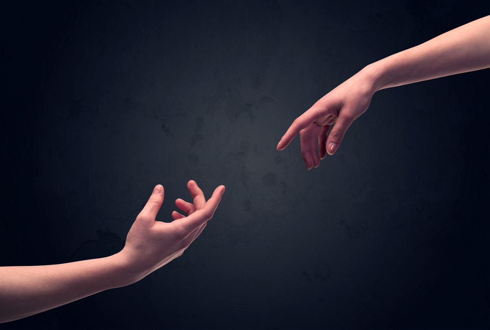 Two male hands reaching out to one another, almost touching, in front of dark clear empty background wall concept