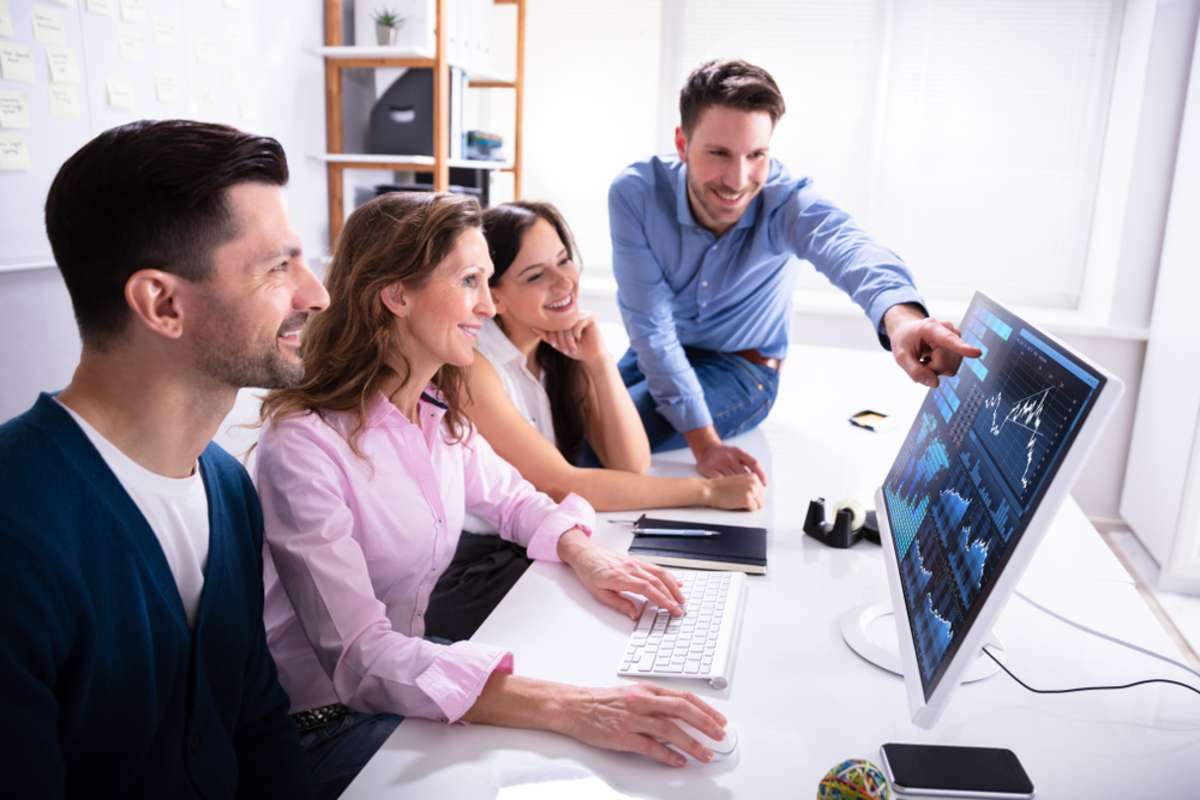 Young Smiling Businesspeople Showing Stock Market Broker Analyzing Graph On Computer At Workplace