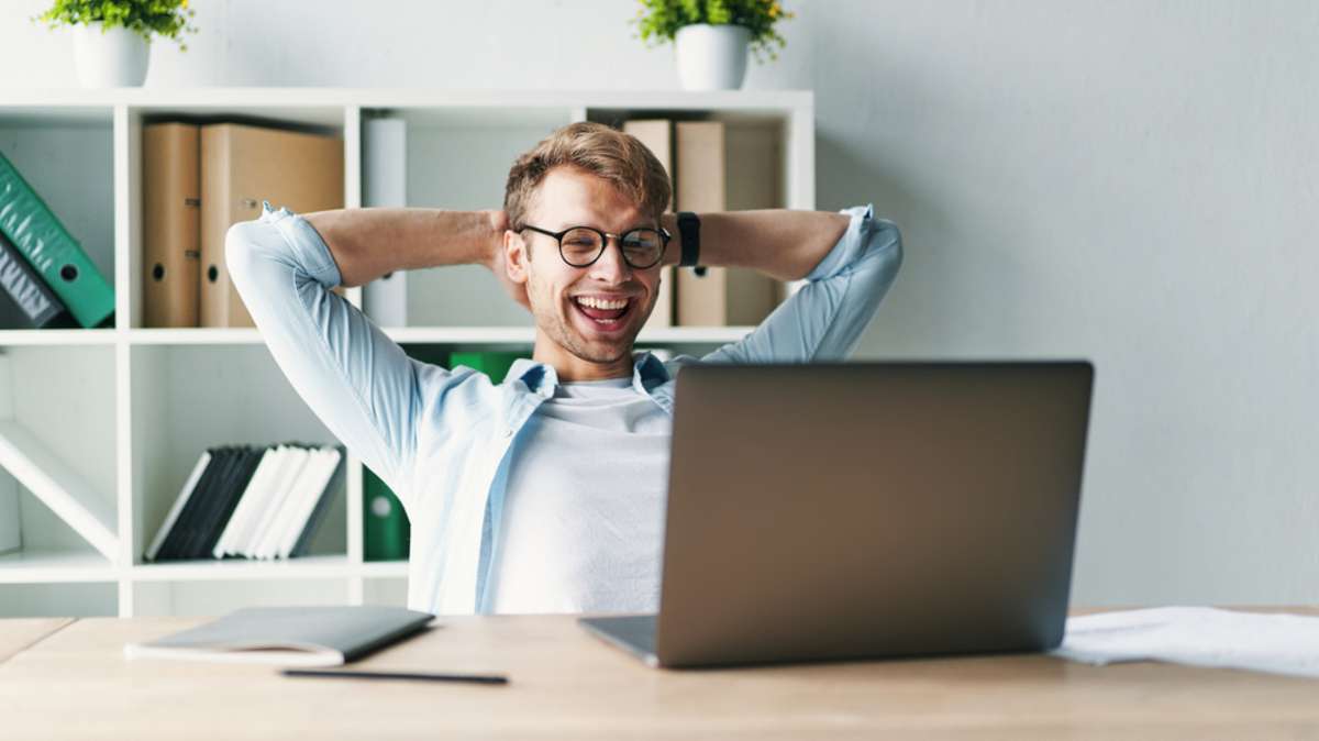 Young man smiling as he reads the screen of a laptop computer while relaxing working on a comfortable place by the wooden table at home